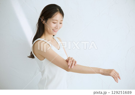 肌に触れてスキンケアする若い女性の笑顔 – 自然光・白背景 129251689