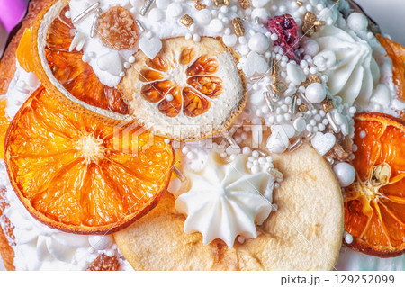 Easter cake decor closeup. Fruitcake decorated dried oranges slices, pears, white meringue, icing, sugar sprinkles. Detail of decorating kulich, top view 129252099