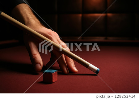Close up of a hand aiming with a cue stick and chalk on a red felt pool table under dramatic low lighting indoors, AI Generative 129252414