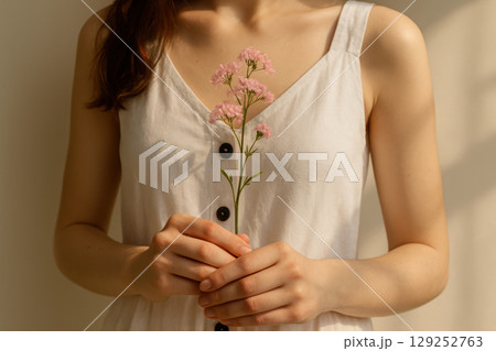 Woman in white sleeveless dress holding delicate pink wildflowers in soft natural light, showcasing gentle simplicity and calm, AI Generative 129252763