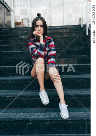 Woman is sitting on a set of stairs in a red and black plaid shirt 129252938