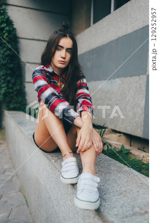 Woman in a red and white plaid shirt sits on a stone wall 129252957