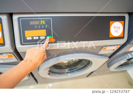 Close-up of female hand selecting washing program on modern washing machine. Choosing laundry mode in public self-service facility. 129253787