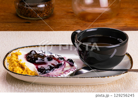 Side view of a cup of coffee in black ceramic cup with blueberry cheese pie on foil paper Side view of a cup of coffee in black ceramic cup with blueberry cheese pie on foil paper 129256245