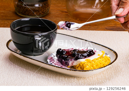 Taking a bite of blueberry cheese pie in white ceramic tray with black coffee in black ceramic coffee cup. Taking a bite of blueberry cheese pie in white ceramic tray with black coffee in black ceramic coffee cup. 129256246
