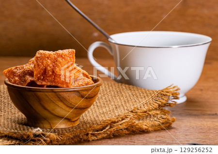 Crispy sweet pork slices in wooden bowl on sack cloth and a white ceramic coffee cup. 129256252