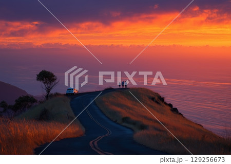 Silhouetted family gazes at glowing ocean sunset from quiet hilltop road 129256673