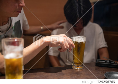 落ち込む後輩にビールを勧める先輩 129256763