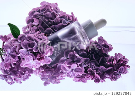 A bottle of serum with petals in water with lilac flowers. A bottle of serum with petals in water with lilac flowers. 129257845