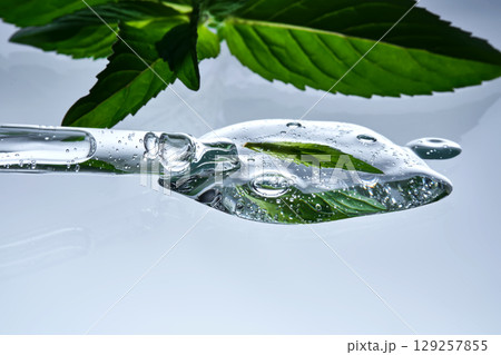 A pipette with a drop of serum in refreshing mint leaves. A pipette with a drop of serum in refreshing mint leaves. 129257855