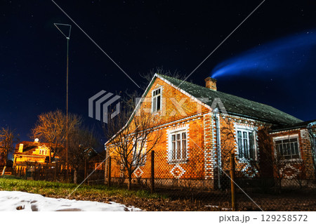 A cozy house in a winter night scene, with a wisp of smoke rising from the chimney. The dark sky is filled with brilliant stars, creating a serene and inviting atmosphere 129258572