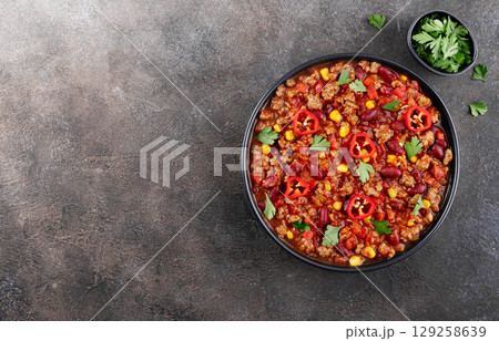 Chili con carne with fresh herbs and nachos chips on a gray background. Top view. Mexican cuisine. Copy space Chili con carne with fresh herbs and nachos chips on a gray background. Top view. Mexican cuisine. Copy space 129258639