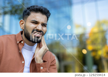 An Indian man is experiencing a painful toothache, expressing discomfort by touching his cheek. 129259414