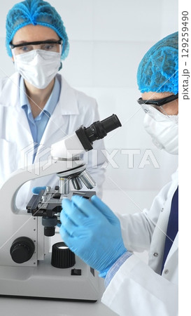 Scientists researchers man and woman in lab coats, masks and goggles conduct research with microscope in laboratory. Concept of medicine and science Scientists researchers man and woman in lab coats, masks and goggles conduct research with microscope in laboratory. Concept of medicine and science 129259490