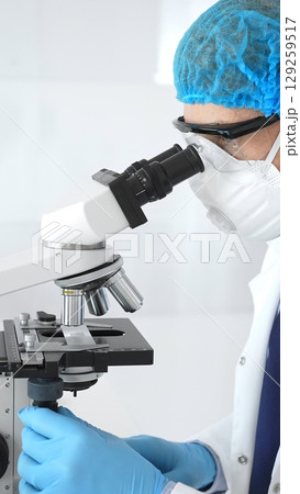 Male senior scientific researcher calibrating precision microscope while examining sample, exploring breakthrough medical research in sterile laboratory setting. Medicine and science concept 129259517