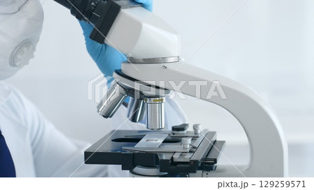 Close up of scientist's hands in blue gloves adjusting microscope in laboratory, conducting scientific research and analysis. Health care and science concept 129259571