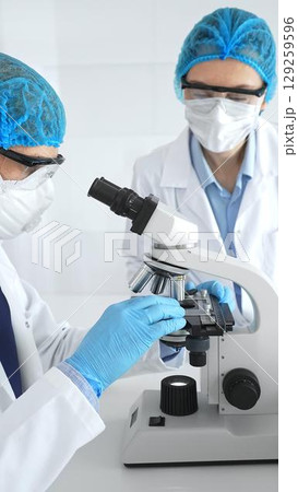 Scientists researchers man and woman in lab coats, masks and goggles conduct research with microscope in laboratory. Concept of medicine and science 129259596