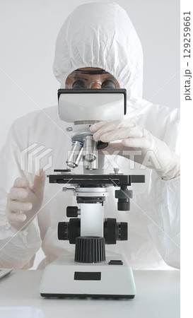 Medical virologist in protective hazmat gear examining viral samples under a microscope while conducting research in a sterile laboratory environment Medical virologist in protective hazmat gear examining viral samples under a microscope while conducting research in a sterile laboratory environment 129259661