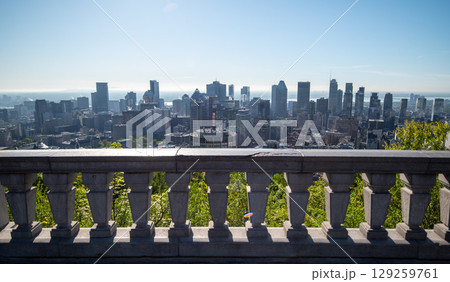 Scenic view of Montreal's skyline showcasing its diverse architecture, with lush green trees in the foreground and the St. Lawrence River in background. 129259761