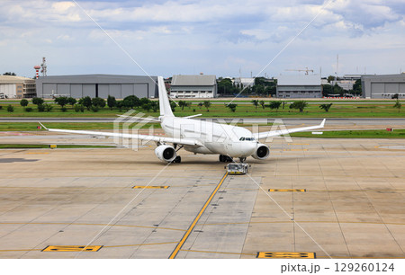 White commercial aircraft are pushed back to the taxiway by airplane tugs, with one in ground handling services 129260124