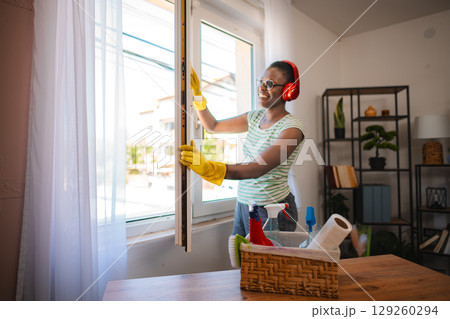 Smiling housekeeper opening window while listening to music with headphones Smiling housekeeper opening window while listening to music with headphones 129260294