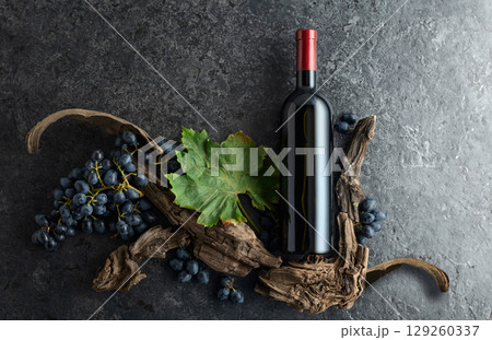 Bottle of red wine, blue grapes, and old vine snags on a black stone background. Bottle of red wine, blue grapes, and old vine snags on a black stone background. 129260337