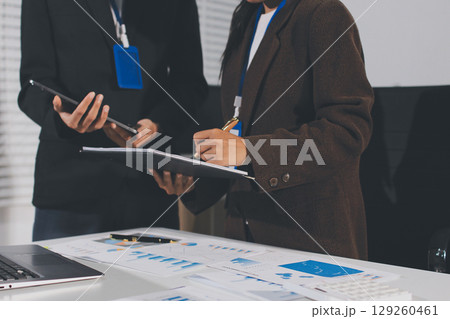 Focused young businessman signing agreement with skilled lawyer in eyeglasses. Concentrated financial advisor showing place for signature on paper contract document to male client at meeting in office Focused young businessman signing agreement with skilled lawyer in eyeglasses. Concentrated financial advisor showing place for signature on paper contract document to male client at meeting in office 129260461