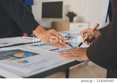 Focused young businessman signing agreement with skilled lawyer in eyeglasses. Concentrated financial advisor showing place for signature on paper contract document to male client at meeting in office 129260485