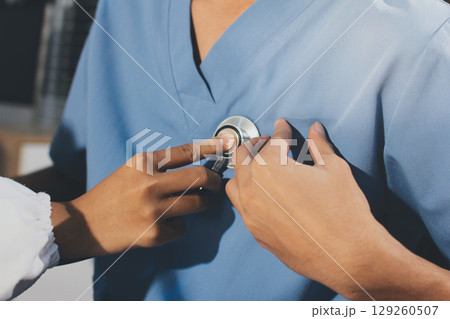 A physician uses a stethoscope to examine a patient's heart during a clinic appointment. 129260507