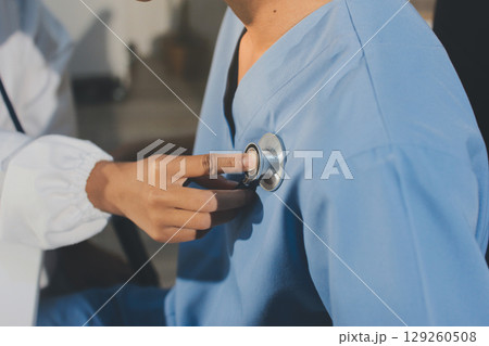 A physician uses a stethoscope to examine a patient's heart during a clinic appointment. 129260508
