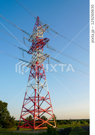 Red and white high-voltage transmission tower against blue sky in a rural landscape at sunset 129260630