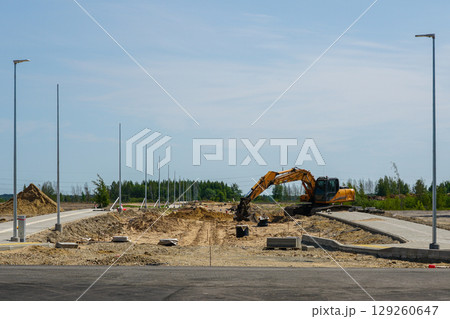 Excavator working at road construction site with light poles and curbs during infrastructure upgrade 129260647