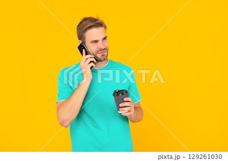 man in shirt speaking on smartphone with morning coffee on yellow background, phone call man in shirt speaking on smartphone with morning coffee on yellow background, phone call 129261030