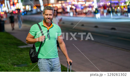 Summer trip in America. Mature tourist in night Miami. Traveler man in casual clothes with suitcase. Man travel abroad weekend. Travel lifestyle. Tourist in summer city. Travel bag, copy space 129261302