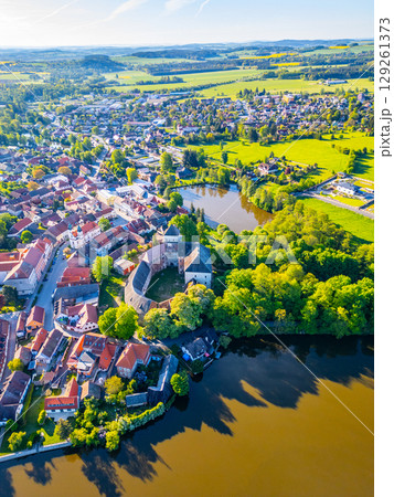Overlooking Rozmital pod Tremsinem, this aerial view captures the charming town, ancient castle, and surrounding lush greenery reflecting on the serene waters below, showcasing a peaceful landscape. Overlooking Rozmital pod Tremsinem, this aerial view captures the charming town, ancient castle, and surrounding lush greenery reflecting on the serene waters below, showcasing a peaceful landscape. 129261373