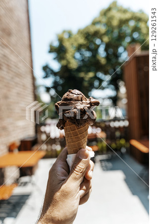 Chocolate Ice Cream Cone in Hand on a Summer Day Chocolate Ice Cream Cone in Hand on a Summer Day 129261543
