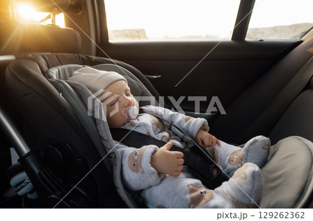 Baby sleeping in an infant car seat, safety travelling by car with little child. Little baby fastened with seat belt in safety car seat. Road trip lifestyle child care transportation rear-facing. 129262362