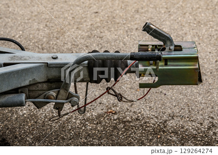Trailer Hitch Coupling Mechanism On Paved Surface: Close-Up Of Metal Tow Bar With Brake Cable, Rubber Sleeve, And Mounting Hardware For Towing Connection 129264274
