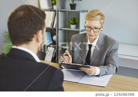 Serious woman in suit conducting hr interview meeting with candidate man, holding clipboard hiring 129266366