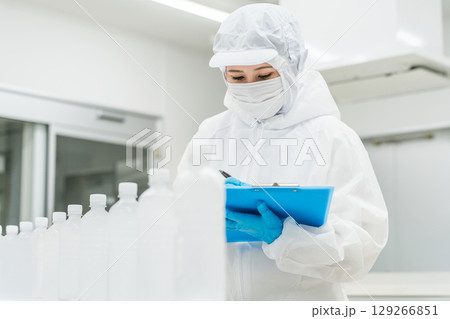 水工場,飲料メーカーで働くペットボトルの水をチェックする防塵服姿の製造スタッフ（飲料メーカー） 129266851