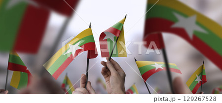 Myanmar flags in their hands on a blurred urban background Myanmar flags in their hands on a blurred urban background 129267528