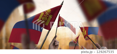 Mongolia flags in their hands on a blurred urban background Mongolia flags in their hands on a blurred urban background 129267535