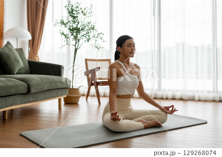 Young Asian woman meditating in lotus position at home Young Asian woman meditating in lotus position at home 129268074