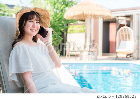 プルサイドのリクライニングチェアに座りスマホで通話する若いアジア人女性(予約,検索,ルームサービス) プルサイドのリクライニングチェアに座りスマホで通話する若いアジア人女性(予約,検索,ルームサービス) 129269328