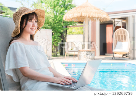 プールサイドのリクライニングチェアに座りパソコンを操作する若いアジア人女性 プールサイドのリクライニングチェアに座りパソコンを操作する若いアジア人女性 129269759