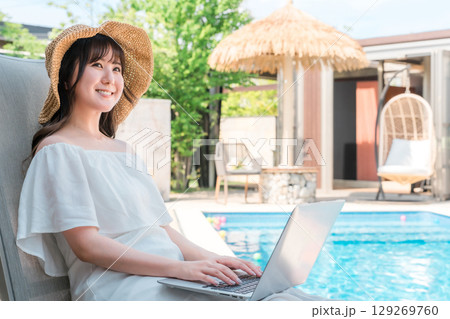 プールサイドのリクライニングチェアに座りパソコンを操作する若いアジア人女性 プールサイドのリクライニングチェアに座りパソコンを操作する若いアジア人女性 129269760