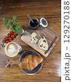 French breakfast featuring golden croissant nestled on rustic wooden board, paired with cranberry cheese, blueberry jam, artisan cappuccino, cherry tomatoes, mint, true French breakfast indulgence. 129270188