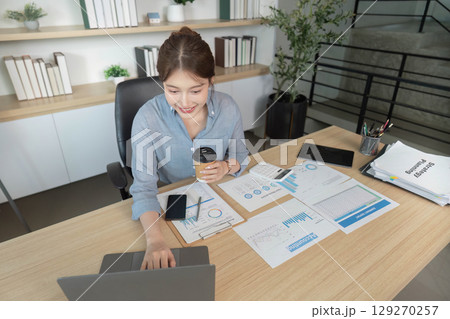 Remote Work. Professional woman multitasking with laptop and coffee in modern office. 129270257