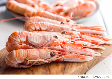 Scampi langoustine on cutting board on white table. Scampi langoustine on cutting board on white table. 129270289