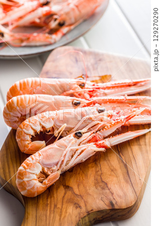 Scampi langoustine on cutting board on white table. Scampi langoustine on cutting board on white table. 129270290